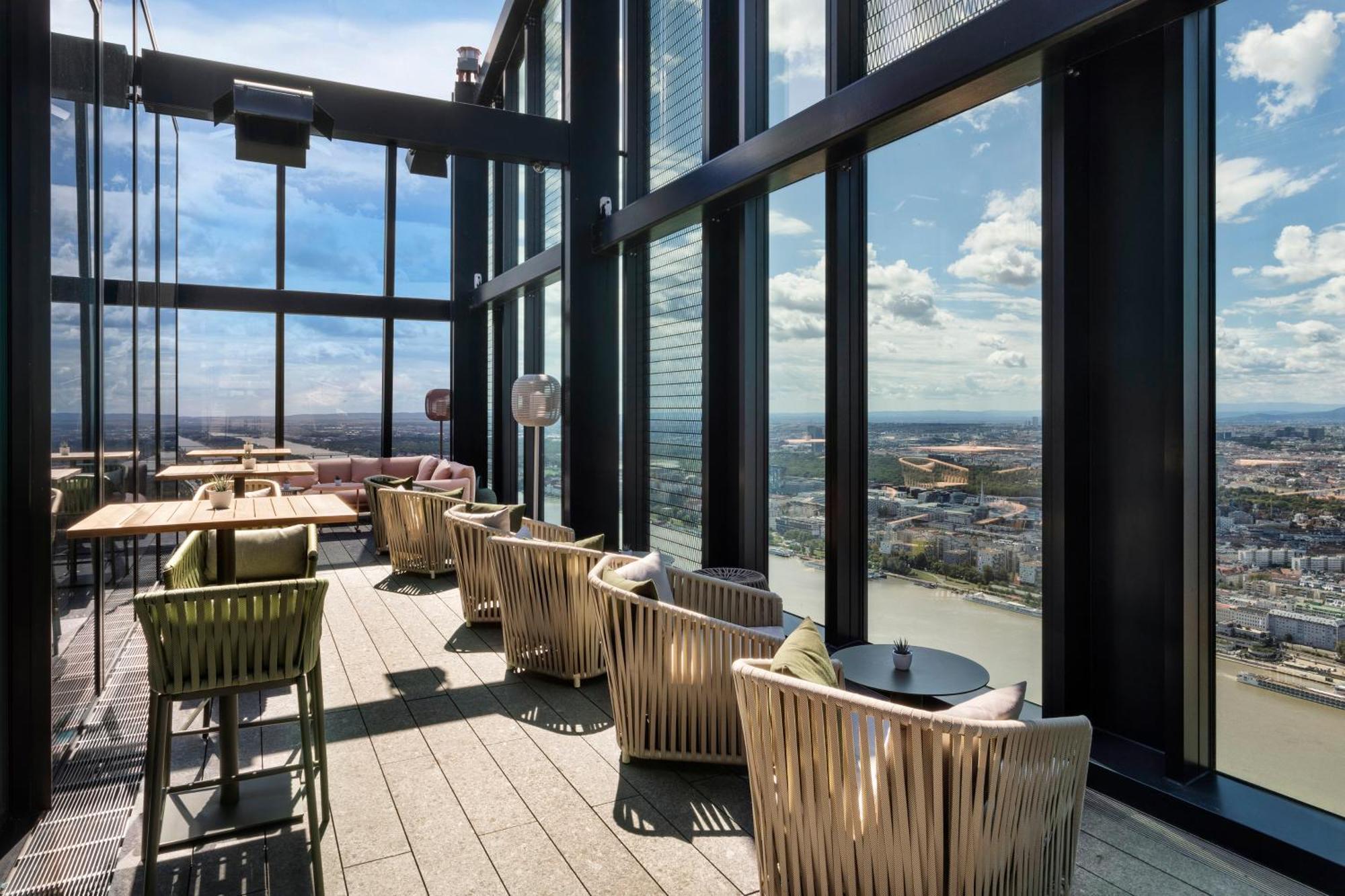 Hotel Melia Vienna Esterno foto The image shows a stylish indoor space with large floor-to-ceiling windows that provide a panoramic view of the landscape outside. The area features several comfortable seating arrangements, including modern chairs and small tables. The design is sle