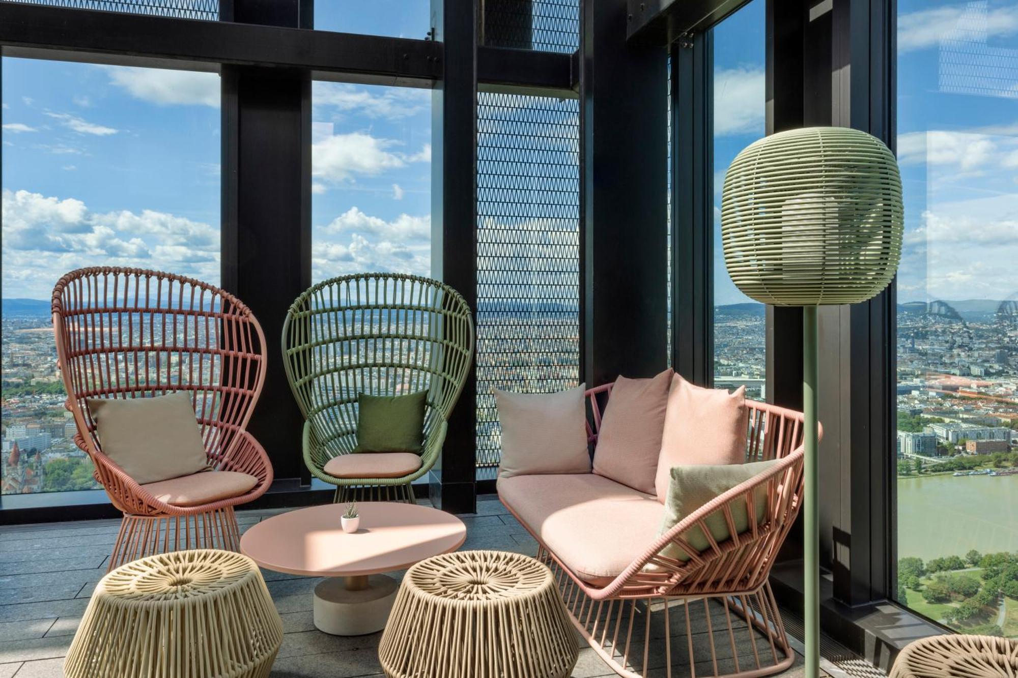 Hotel Melia Vienna Esterno foto The photo shows a modern lounge area with large windows offering a view of the outdoors. There are two stylish, high-backed chairs made of wicker in pastel colors—one pink and one green. A cozy sofa in a soft pink hue is positioned between them, acco