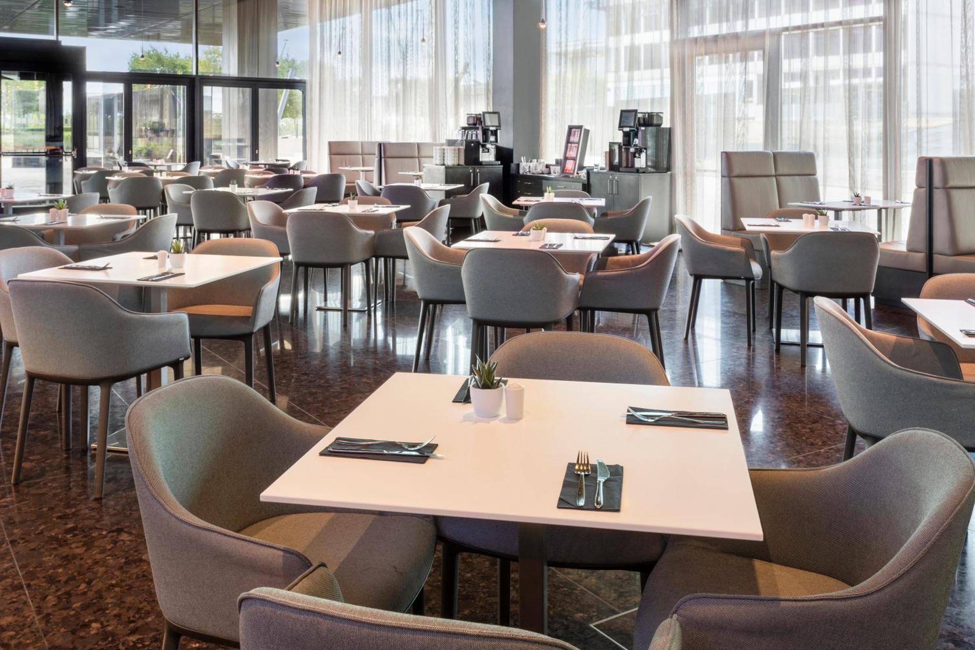 Hotel Melia Vienna Esterno foto The photo shows a spacious dining area in a restaurant or café. There are several tables arranged throughout the space, each with light-colored tabletops and comfortable chairs. The decor appears modern and minimalistic, with large windows allowing n